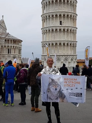 Tomek z flagą Dzikie Życie RunTeam obok Krzywej wieży w Pizie.